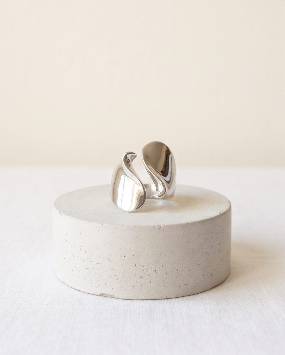 Model's hand in cream linen sleeve wearing silver tone high polish sculptural S-wave open adjustable ring against warm greige wall