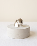 Model's hand in cream linen sleeve wearing silver tone high polish sculptural S-wave open adjustable ring against warm greige wall