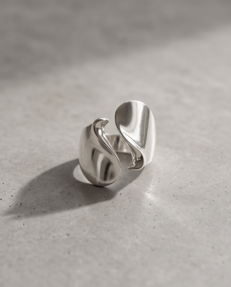 Silver tone high polish sculptural S-wave open adjustable ring standing on concrete surface in natural light showing shadow and sculptural depth