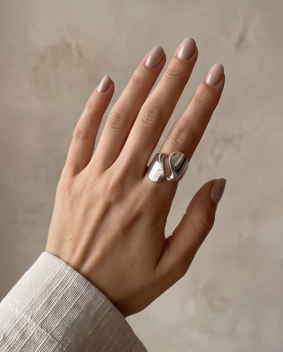 Silver tone high polish sculptural S-wave open adjustable ring displayed on white concrete cylinder plinth against cream background