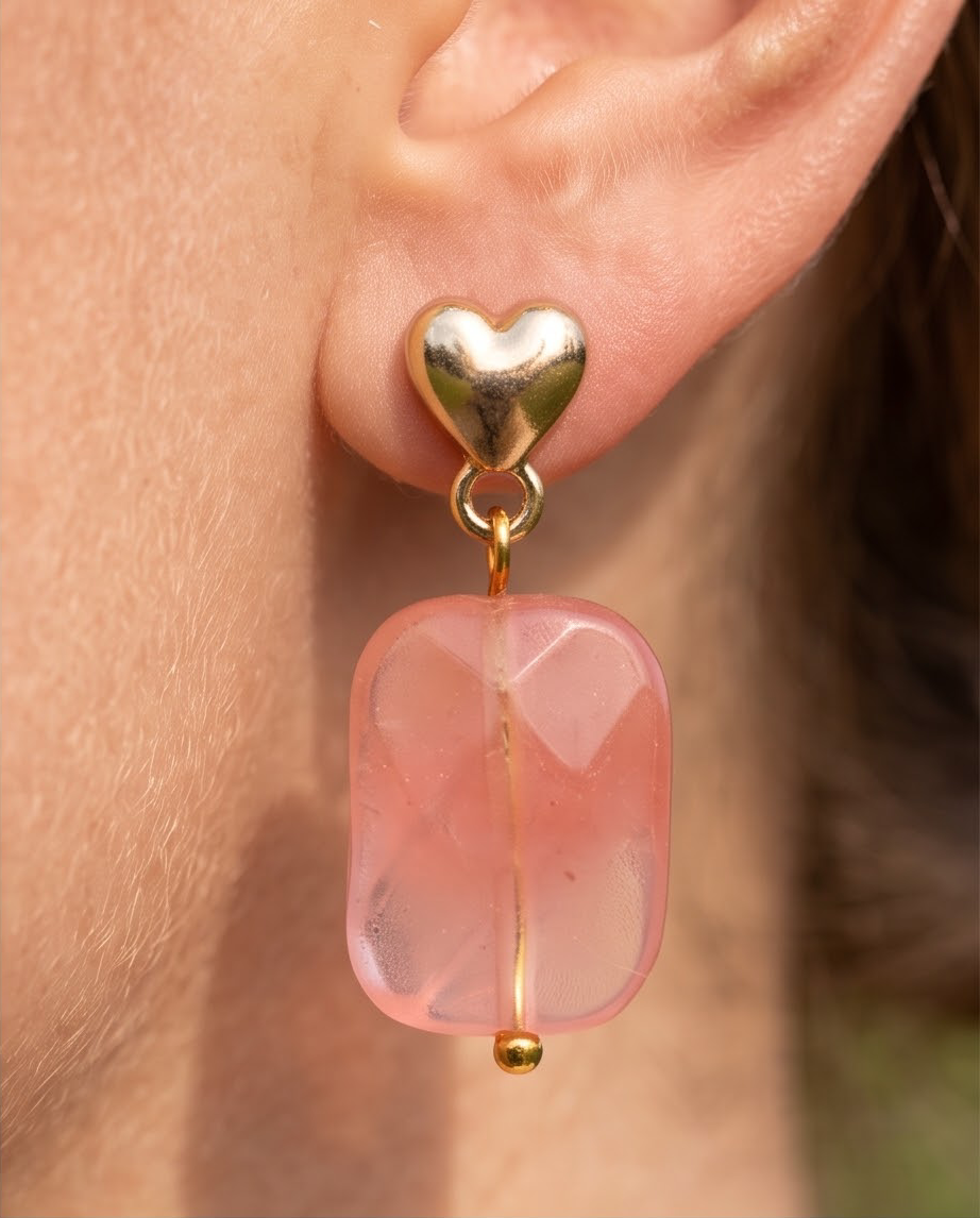 Close up of gold puffed heart stud and faceted pink stone drop earring worn on ear