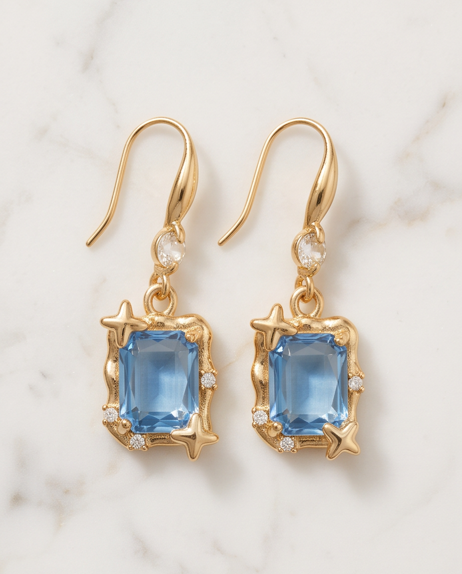 Gold Star Frame Blue Crystal Drop Earrings — flat lay on marble with hook fastening