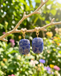Gold heart stud sodalite drop earrings hanging on a gold branch in a garden