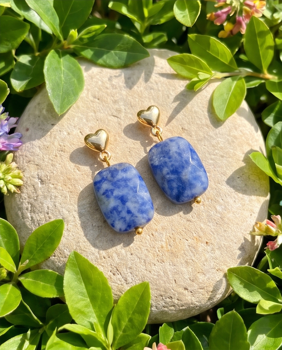 Pair of gold heart stud sodalite drop earrings displayed on a stone in a garden setting