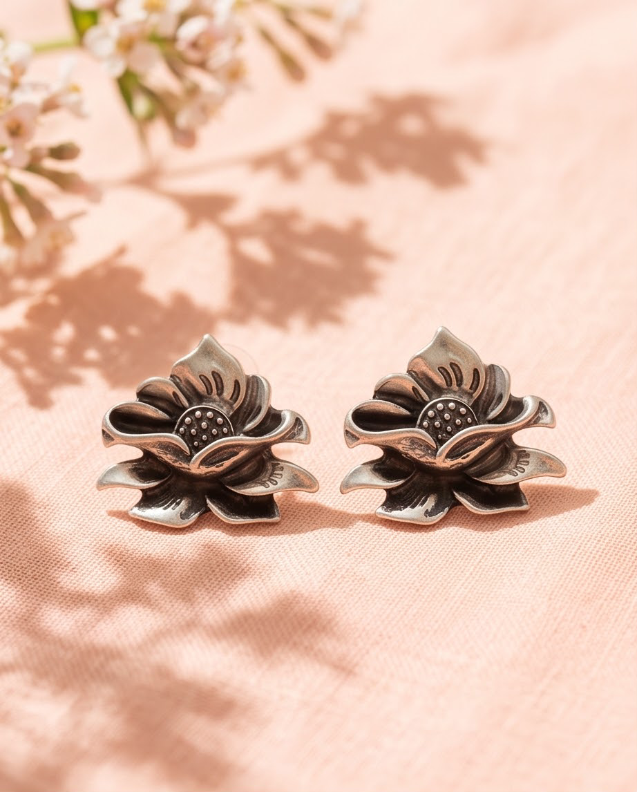 Pair of antique silver lotus flower stud earrings flat lay on blush pink fabric with white flowers