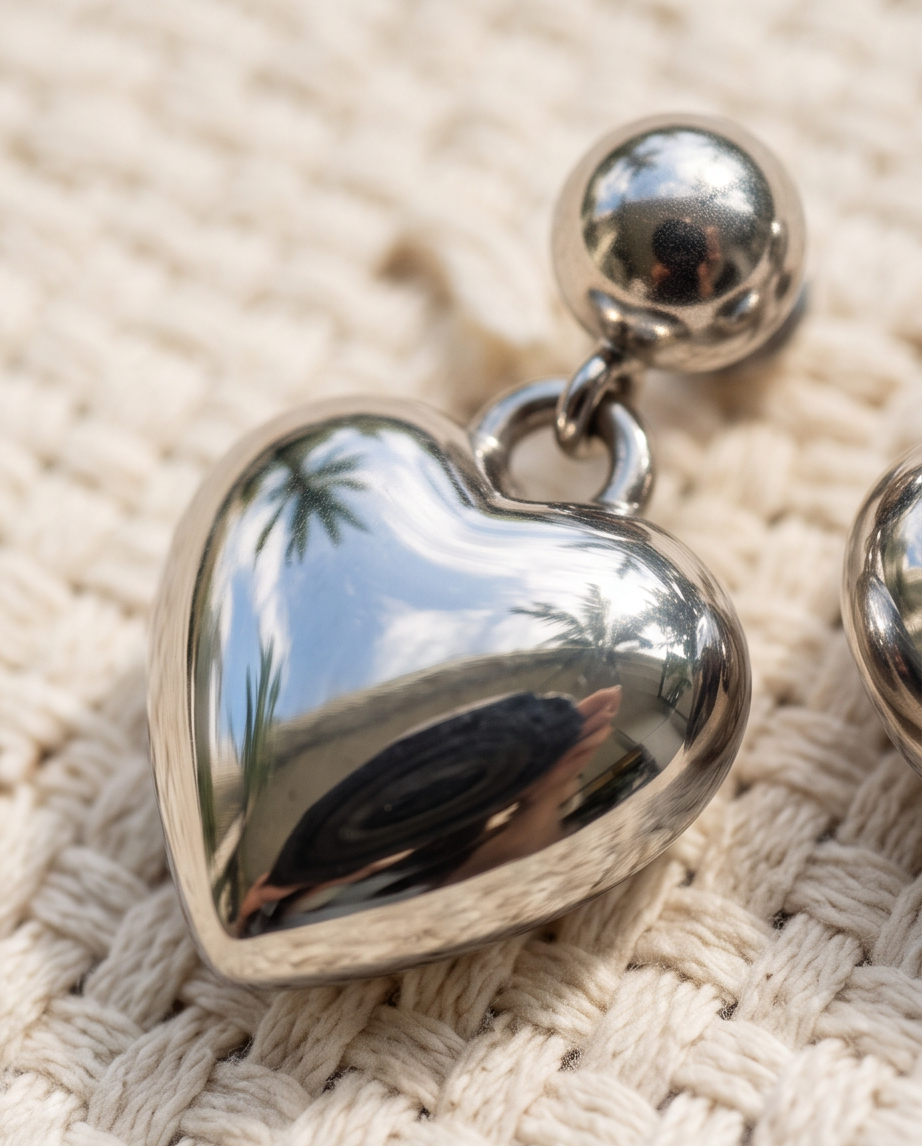 Pair of silver puffed heart ball stud drop earrings displayed on travertine stone block