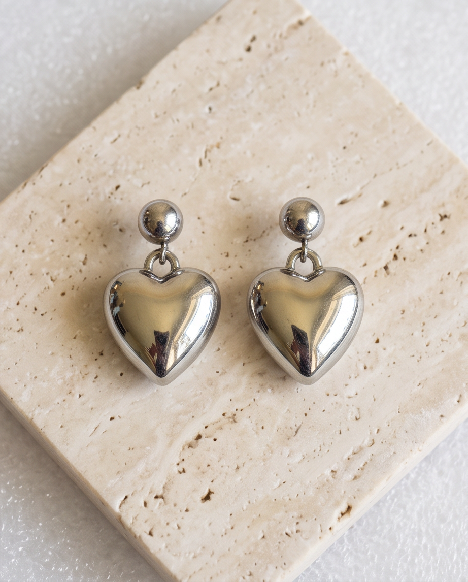 Silver puffed heart ball stud drop earrings laid on weathered wood in golden hour light