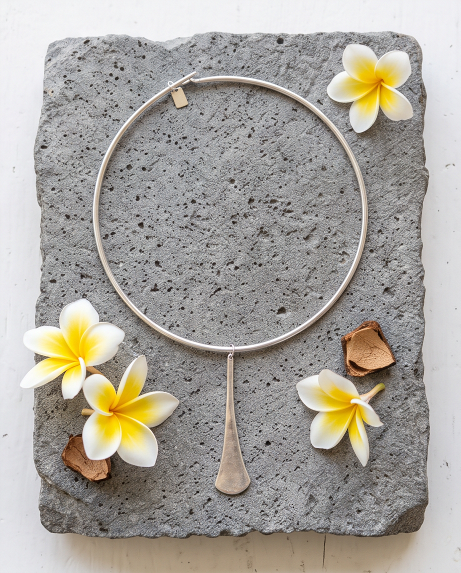 Silver hammered teardrop pendant collar necklace laid flat on volcanic stone with frangipani flowers