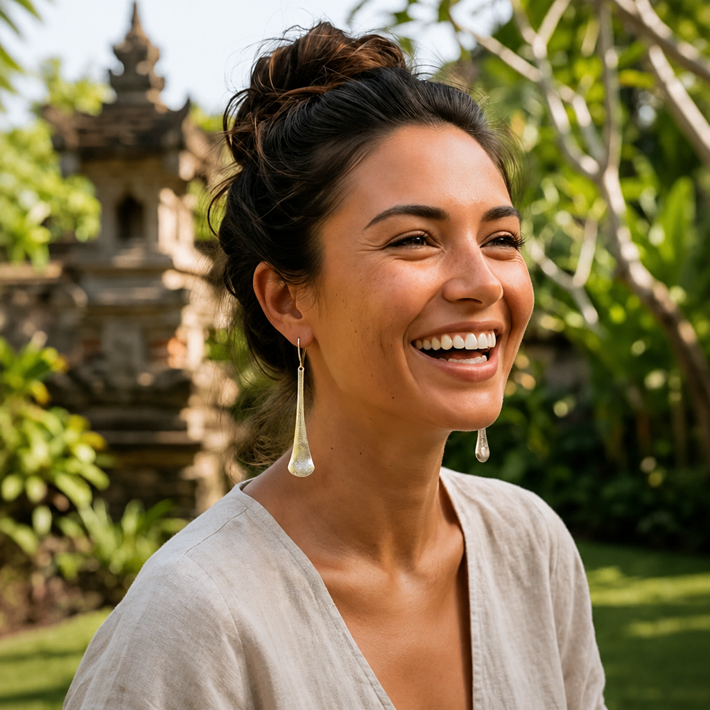 Silver etched elongated teardrop drop earrings hanging on a wooden display with tropical Balinese backdrop