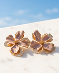 Pair of blush and gold oversized flower stud earrings on marble surface with blue sky