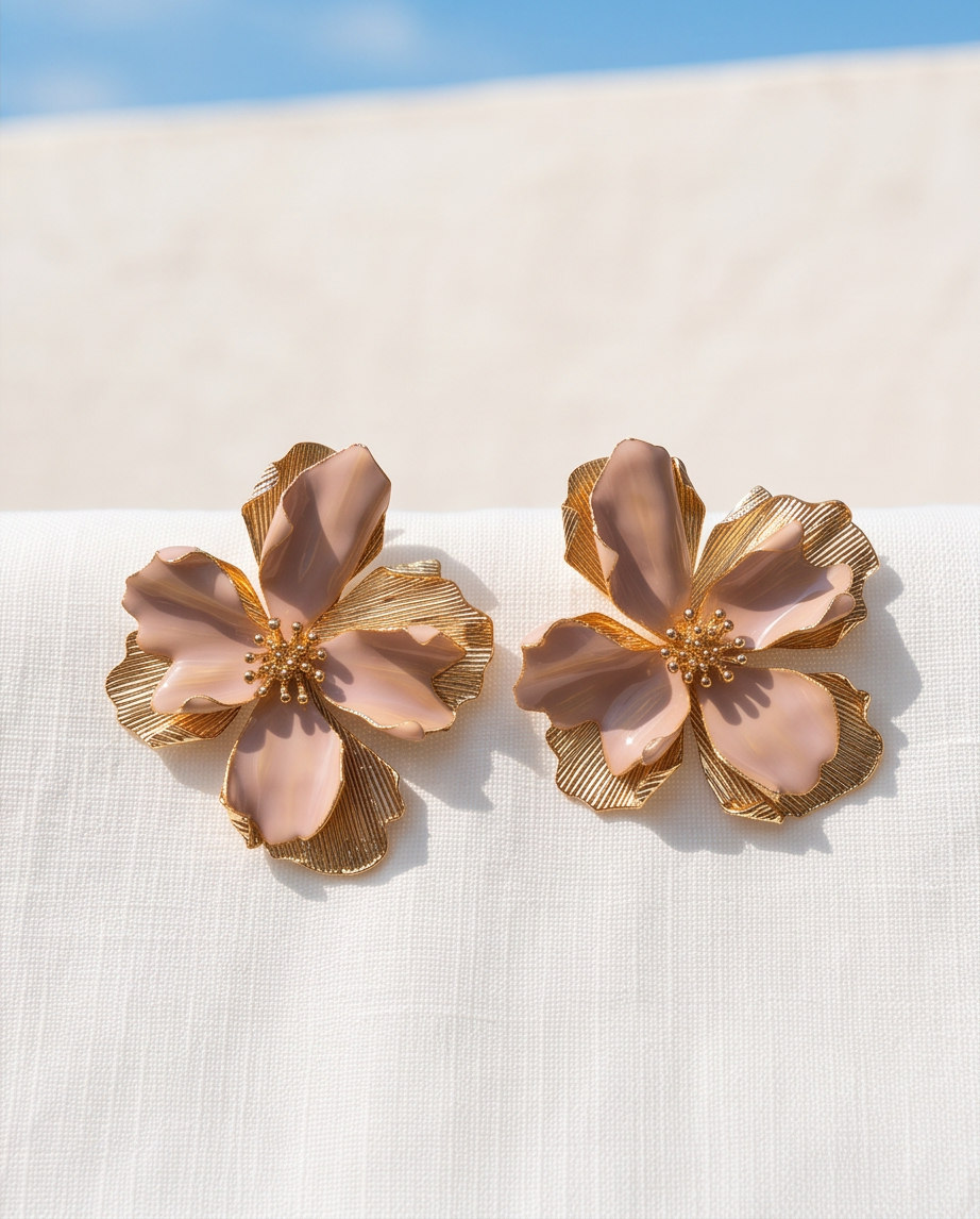 Pair of blush and gold oversized flower stud earrings on white linen