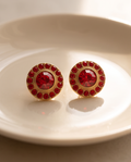 Pair of gold ruby crystal halo stud earrings displayed on white ceramic dish