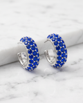 Pair of silver sapphire crystal pavé hoop earrings on white marble surface