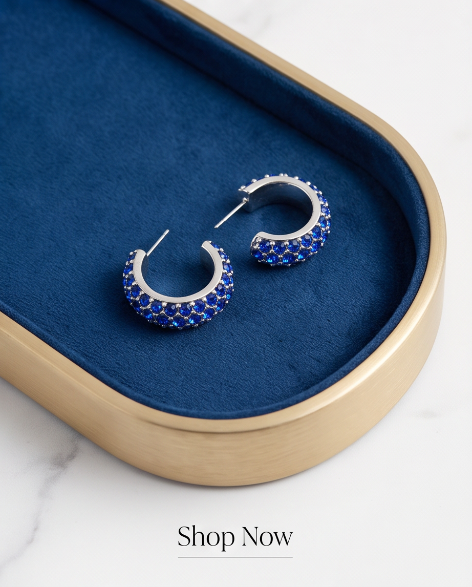 Pair of silver sapphire crystal pavé hoop earrings on navy velvet tray with gold border