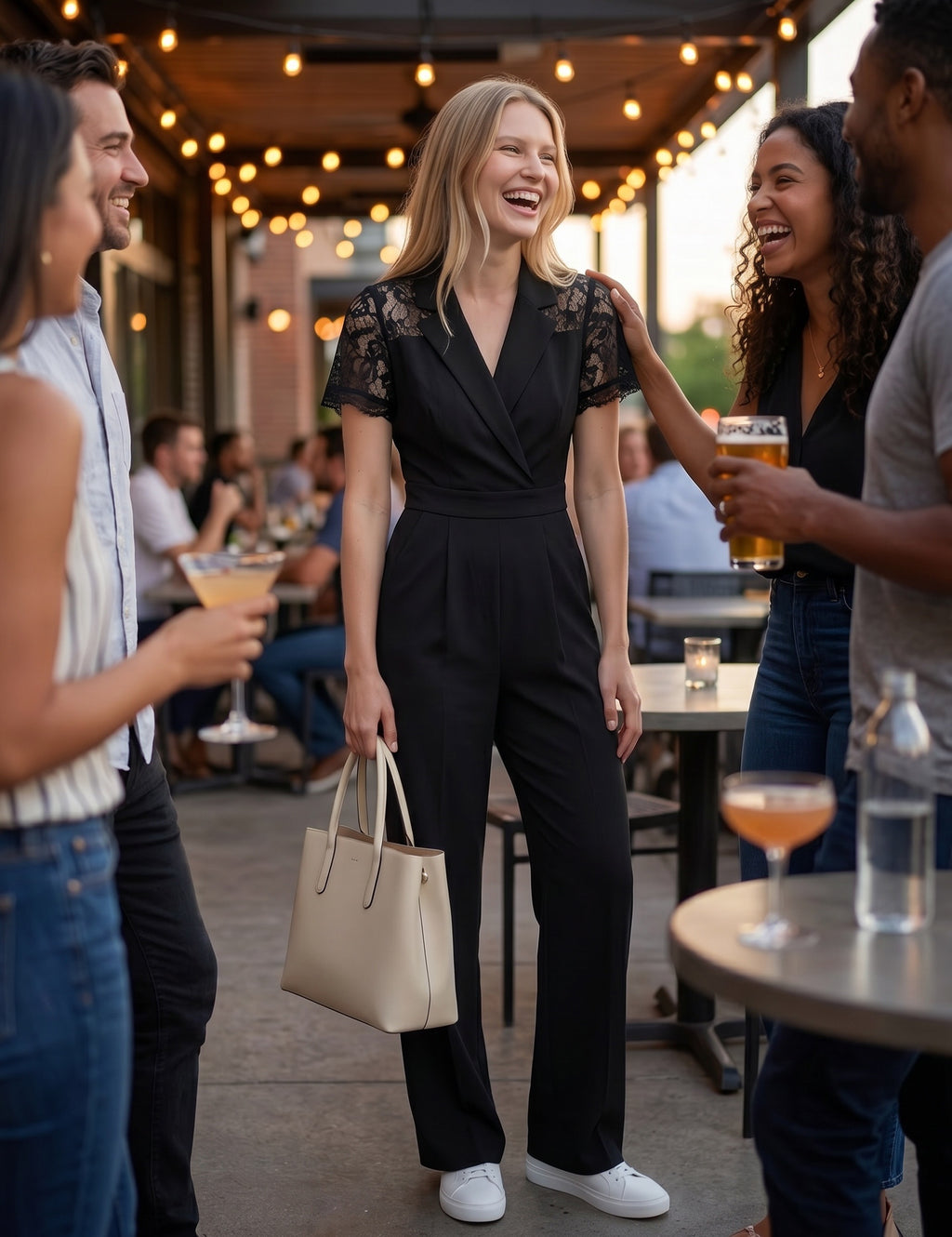 Woman in a black jumpsuit standing among friends at an outdoor social gathering.