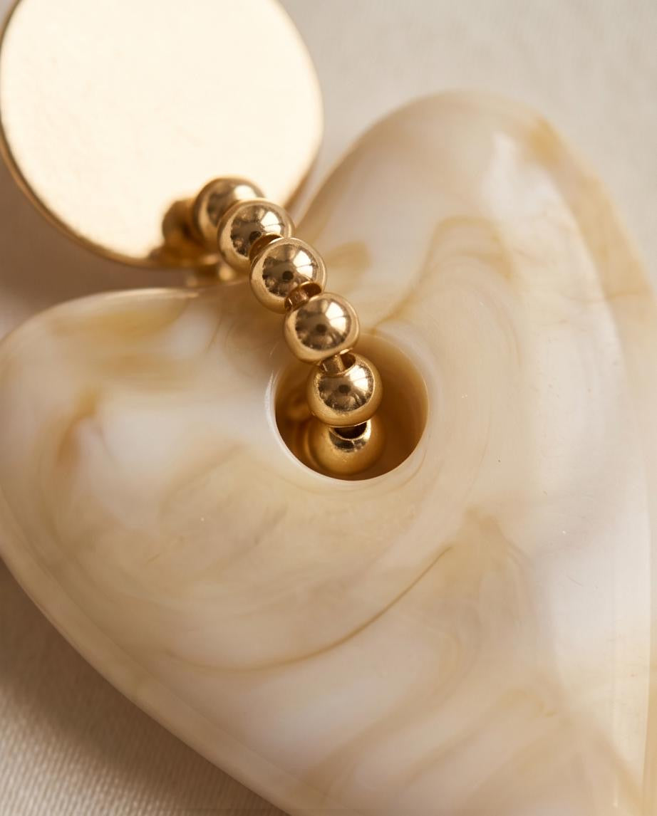 Close-up of gold ball bead connector on cream marble heart earring