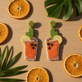 Beaded orange cocktail glass earrings with green cactus leaf and citrus garnish, summer staging shot