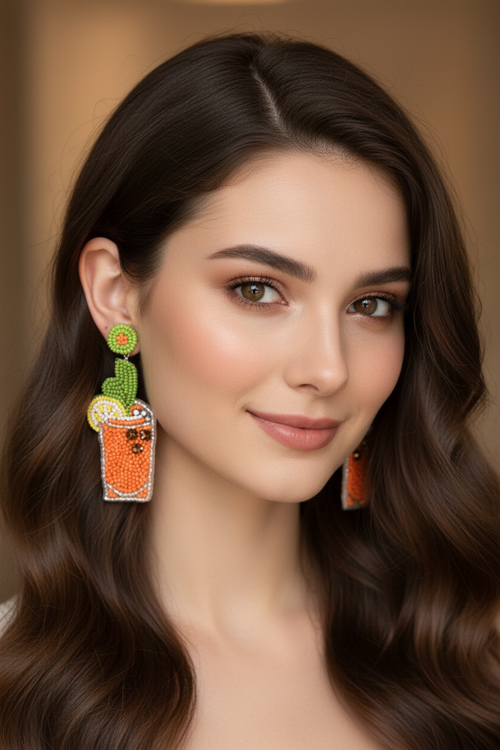 Close-up portrait of model wearing beaded orange cocktail glass earrings with green cactus leaf detail